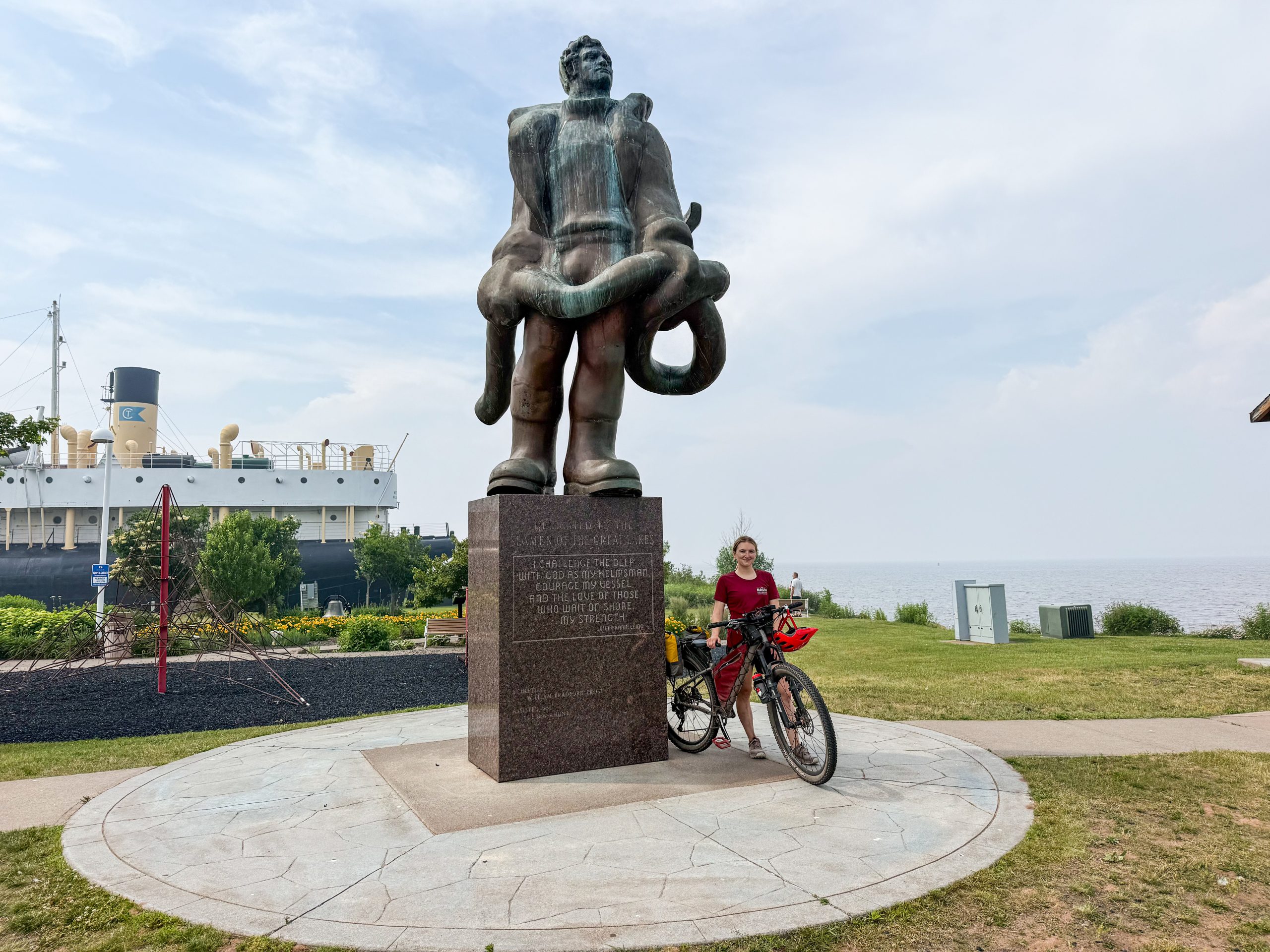 Niina Baum standing alongside a bike next to a statue honoring seaman in Superior, WI.